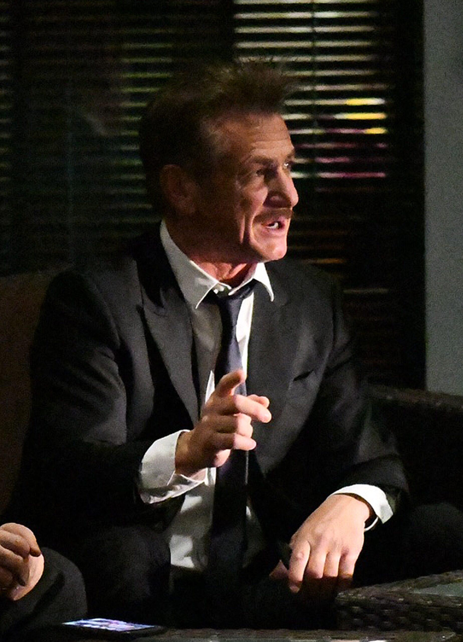 Actor Sean Penn wears a sharp suit and smokes a cigarette as he chats with friends outside his hotel in Miami